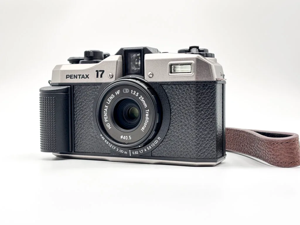 Appareil photo Pentax 17 posé sur fond blanc, vu de face avec son objectif 25mm f/3.5.