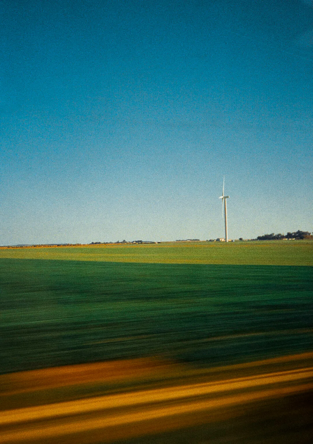 Éolienne au loin photographiée depuis un TGV en mouvement entre Paris et Nantes, avec effet de filé sur les champs.