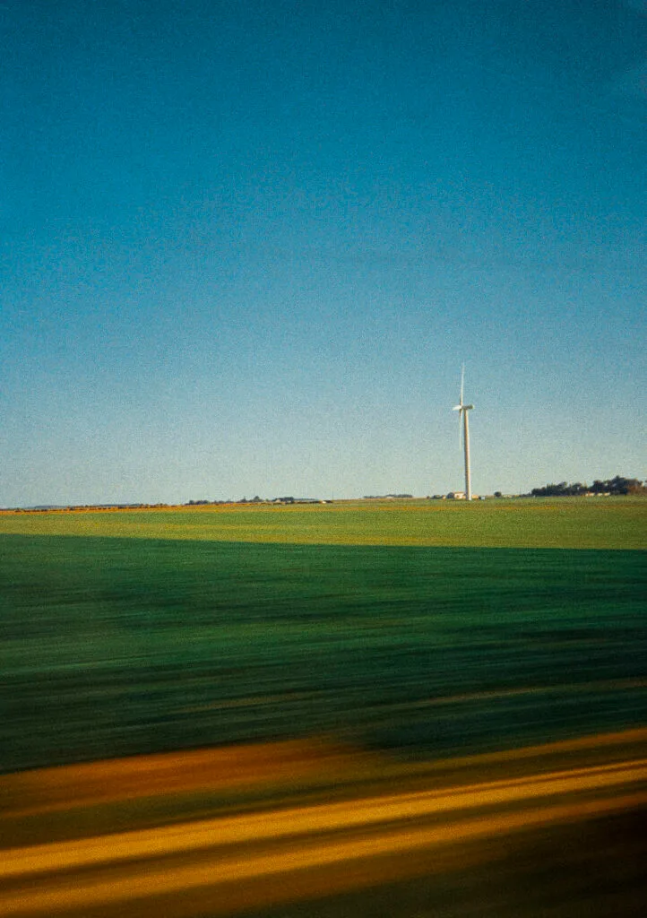 Éolienne au loin photographiée depuis un TGV en mouvement entre Paris et Nantes, avec effet de filé sur les champs.