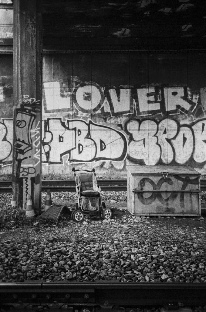 Poussette abandonnée sur une voie ferrée à Nantes, devant un mur recouvert de graffitis colorés, photographiée en noir et blanc.