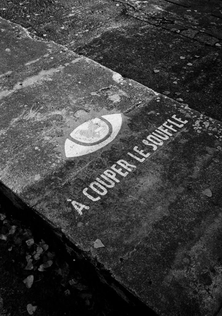Inscription “À couper le souffle” peinte au sol, avec un symbole d’œil stylisé.