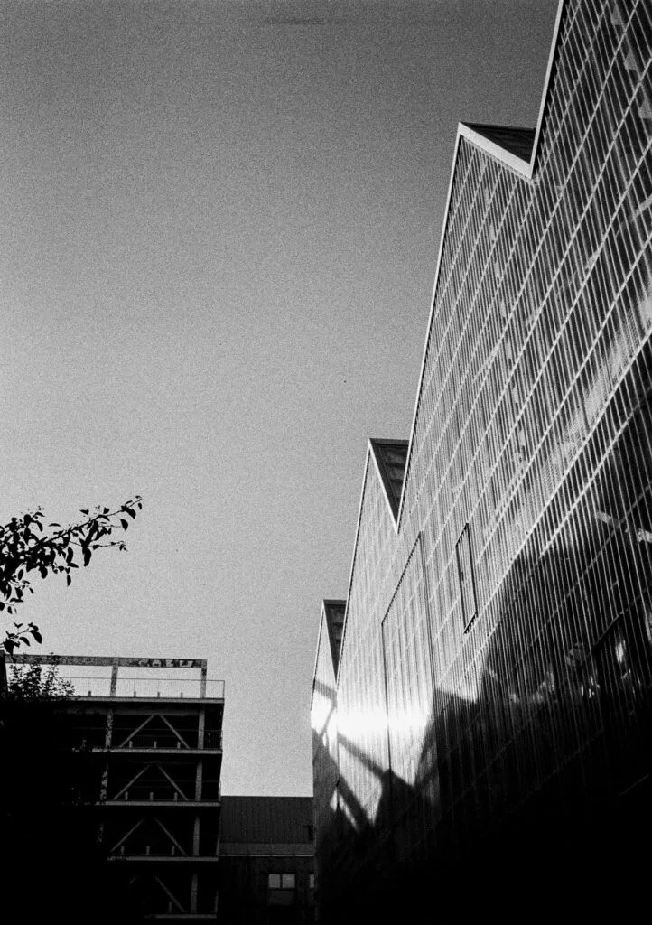 Façade en dents de scie des Halles Alstom à Nantes, photographiée avec ombre portée et ciel dégagé en noir et blanc.