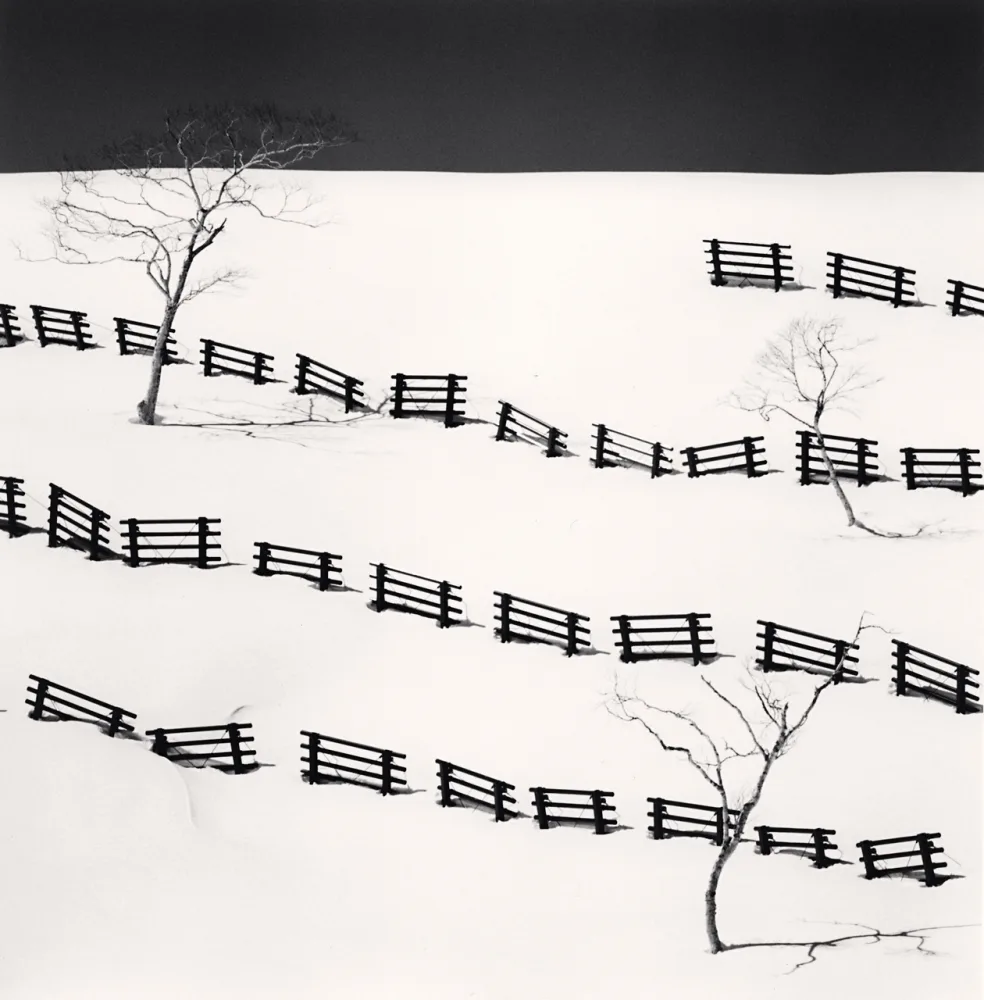 Rangées de barrières noires sur une colline enneigée à Bihoro, Hokkaido, photographiées en noir et blanc par Michael Kenna en 2016.