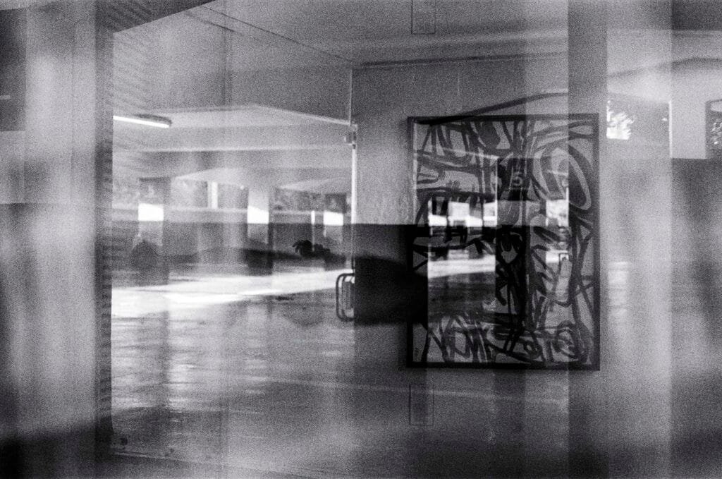 Superposition accidentelle entre une œuvre abstraite du Musée d’Art de Nantes et l’architecture du parking Gare Nord, en noir et blanc sur TMAX 400 périmée.