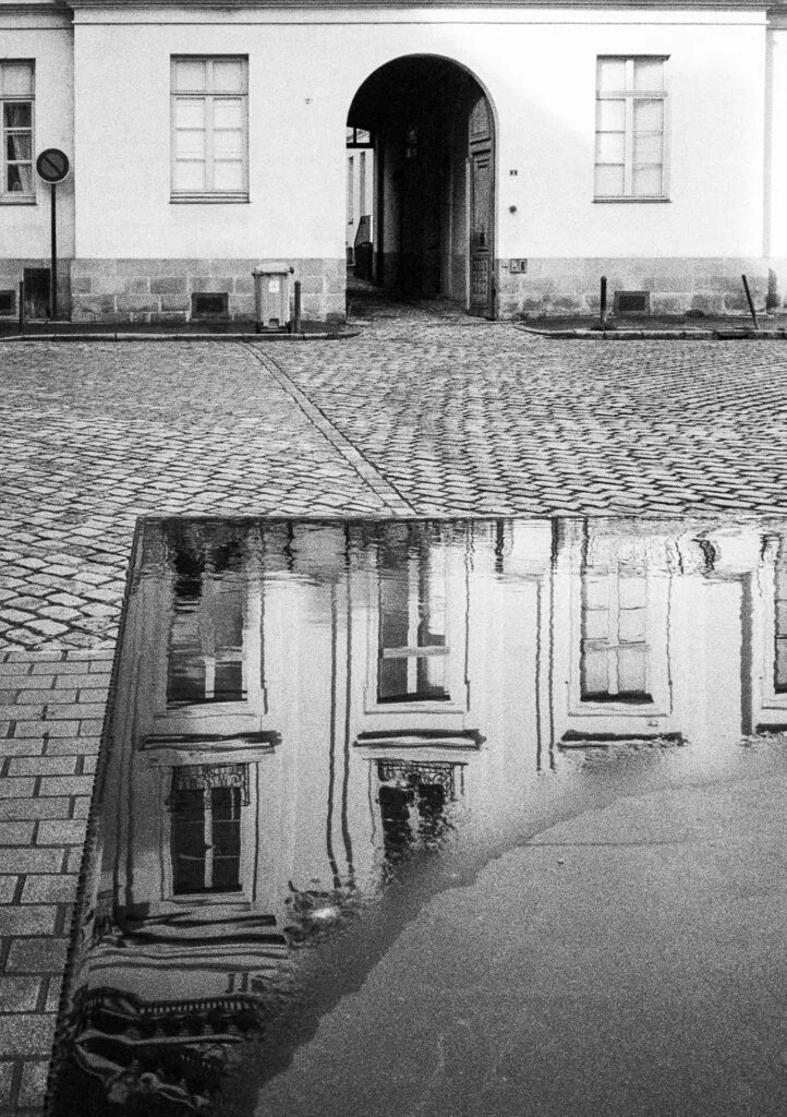 3. Texte alternatif (alt text) Reflet d’un immeuble dans une flaque sur des pavés, dans une cour ancienne de Nantes, photographié en noir et blanc.