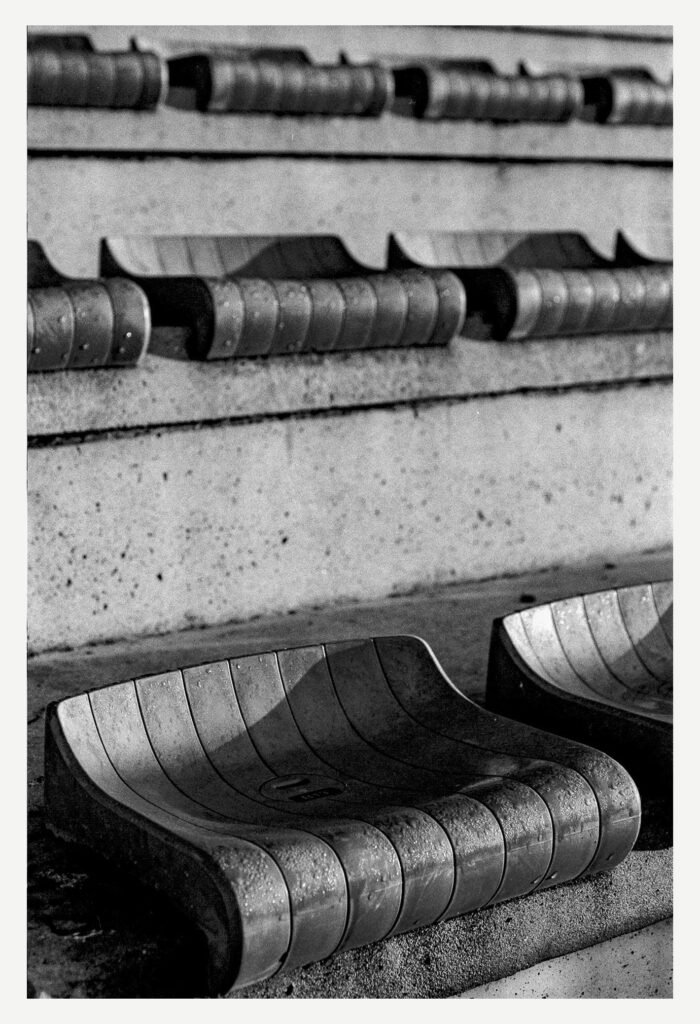 Sièges usés en plastique dans les gradins du stade nantais, photographiés en noir et blanc.