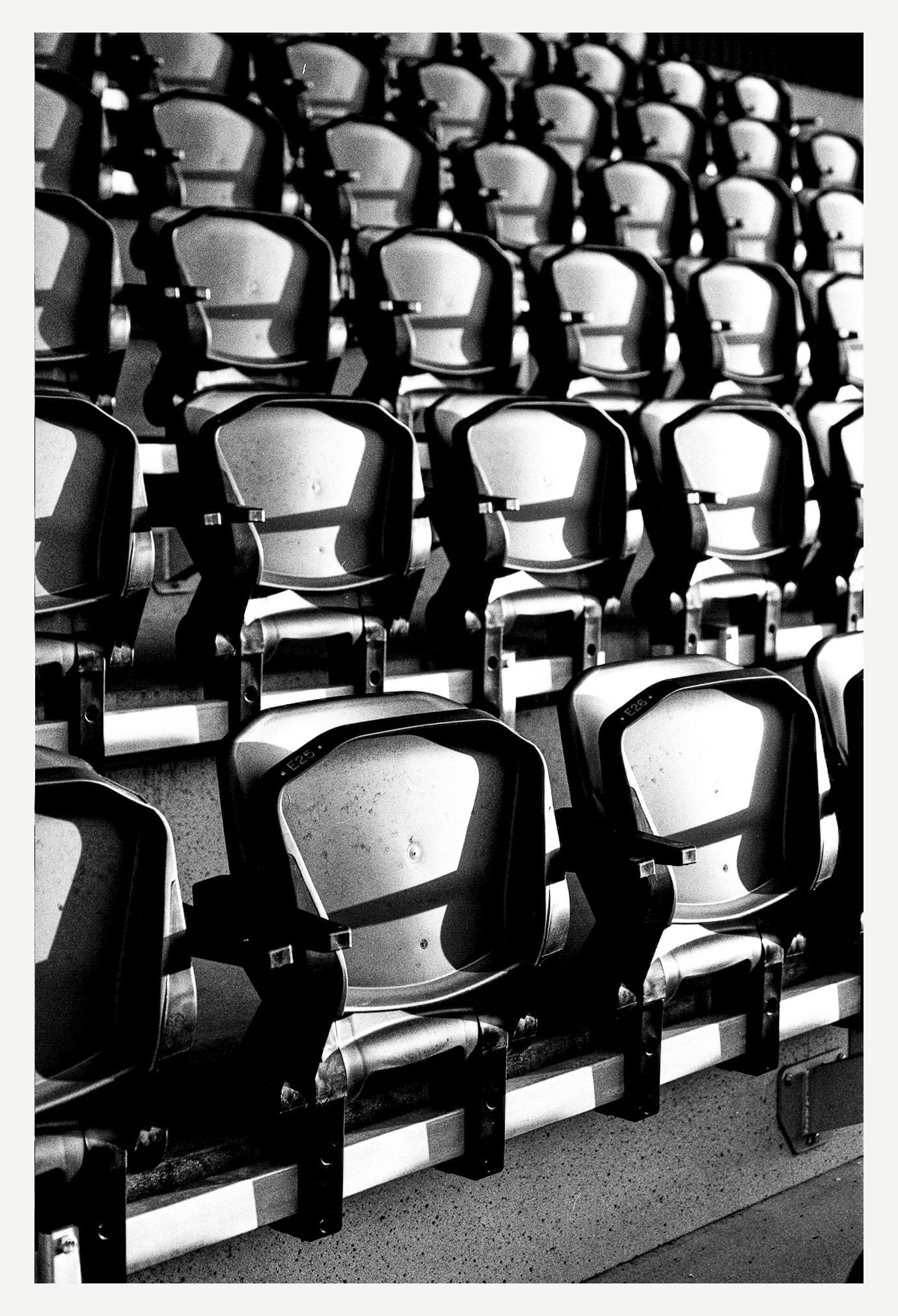 Sièges du stade nantais éclairés par une lumière rasante, en noir et blanc contrasté.