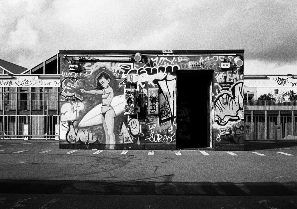 Fresque colorée représentant une surfeuse en bikini, sur un local technique recouvert de graffitis, sur le toit d’un parking à Nantes.