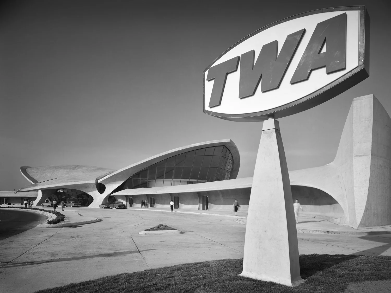 Vue extérieure du TWA Flight Center à New York avec l’enseigne TWA au premier plan, photographiée en 1962 par Ezra Stoller. Architecture fluide d’Eero Saarinen.