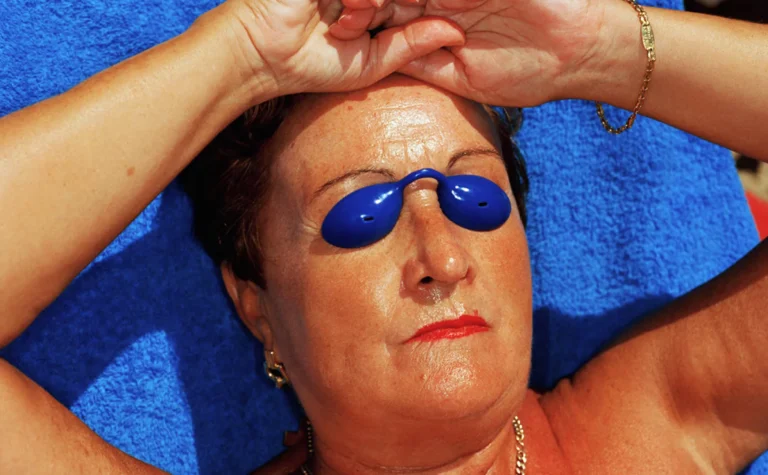 Femme allongée au soleil à Benidorm en 1997, portant des lunettes de bronzage bleues, photographiée par Martin Parr.