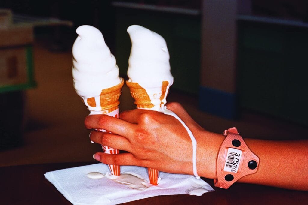 Deux glaces à l’italienne en train de fondre dans la main d’une personne portant un bracelet d’identification rose. Photographie de Martin Parr à Tokyo en 1998.