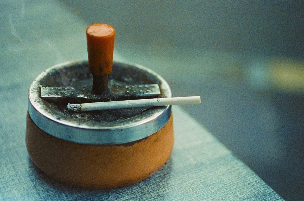 Cendrier orange en métal avec une cigarette posée sur le rebord, photographié à Nantes.