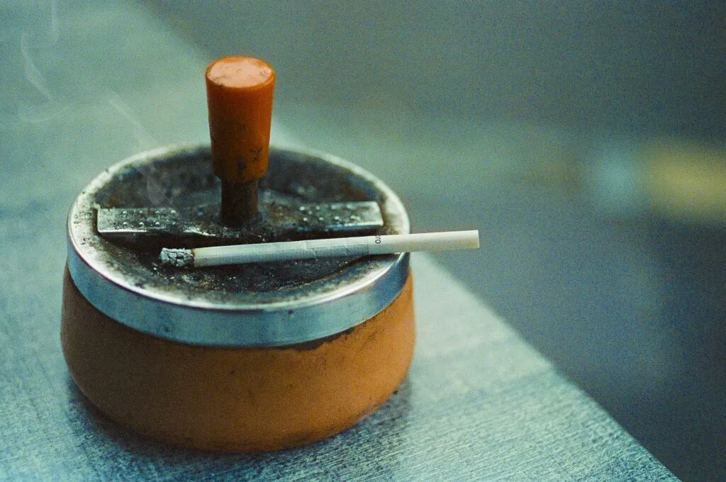 Cendrier orange en métal avec une cigarette posée sur le rebord, photographié à Nantes.