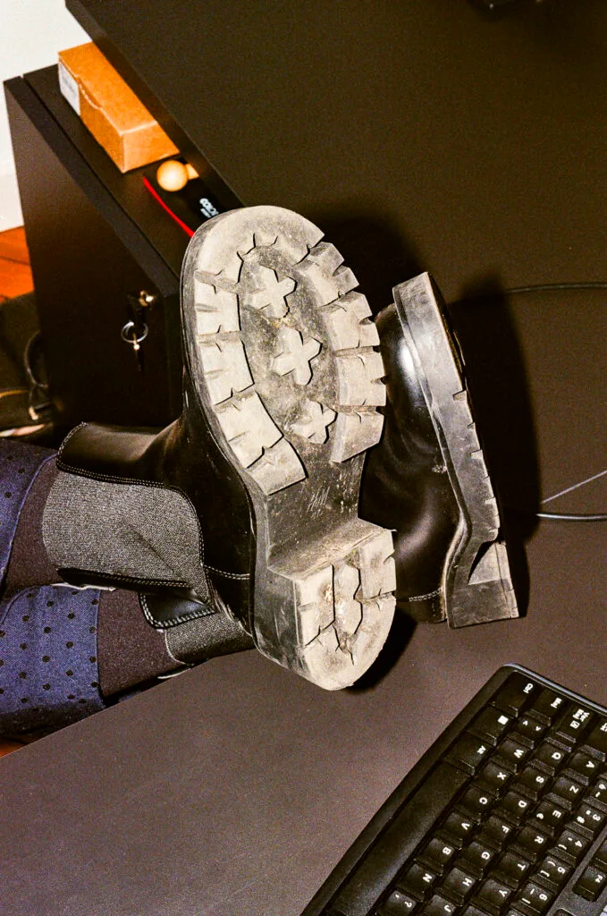 Pieds posés sur un bureau noir, semelles de bottines épaisses en gros plan, éclairées au flash.