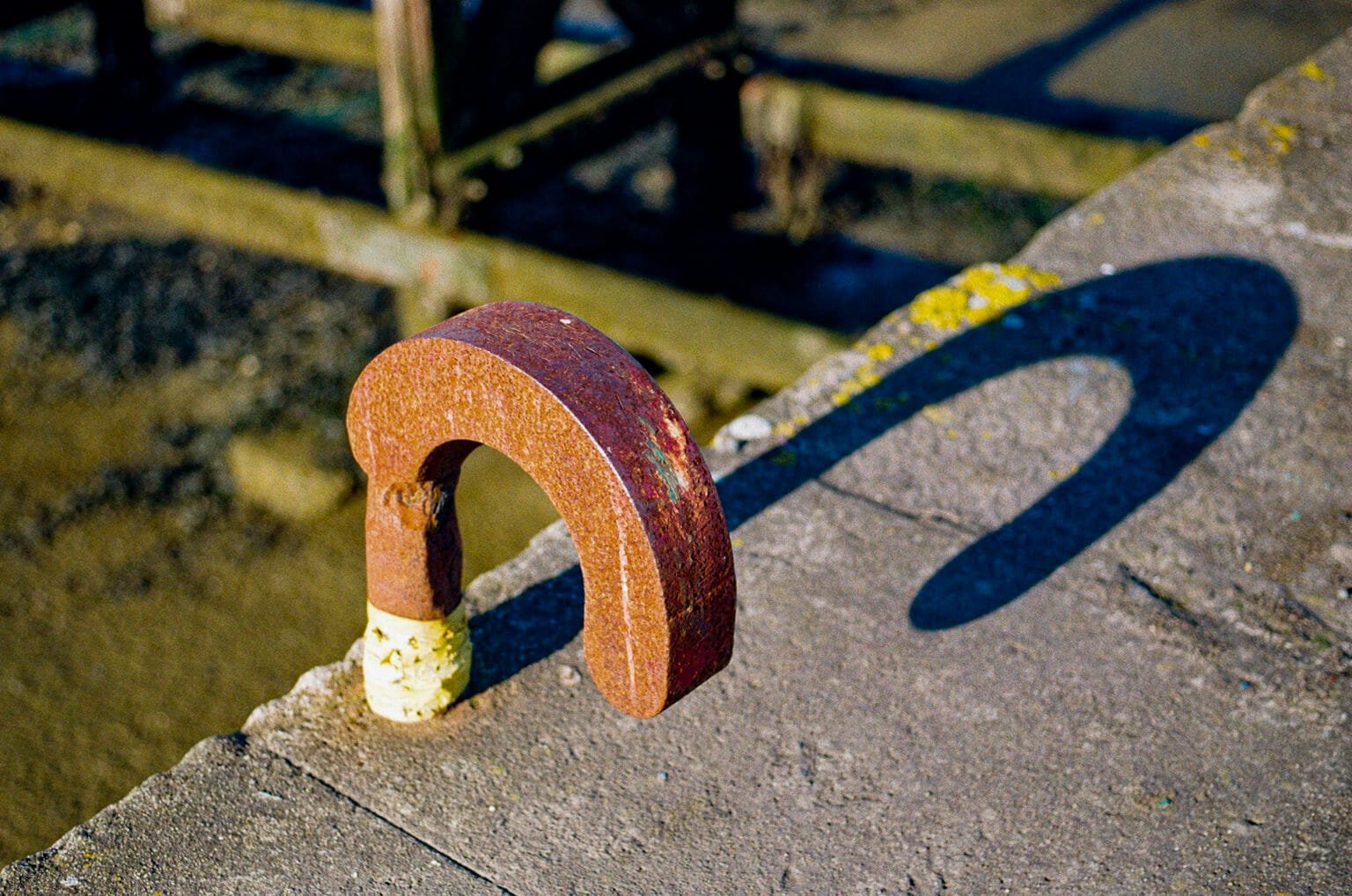 Anneau de métal rouillé sur un quai du port du Croisic, projetant une ombre en forme de point d’interrogation.