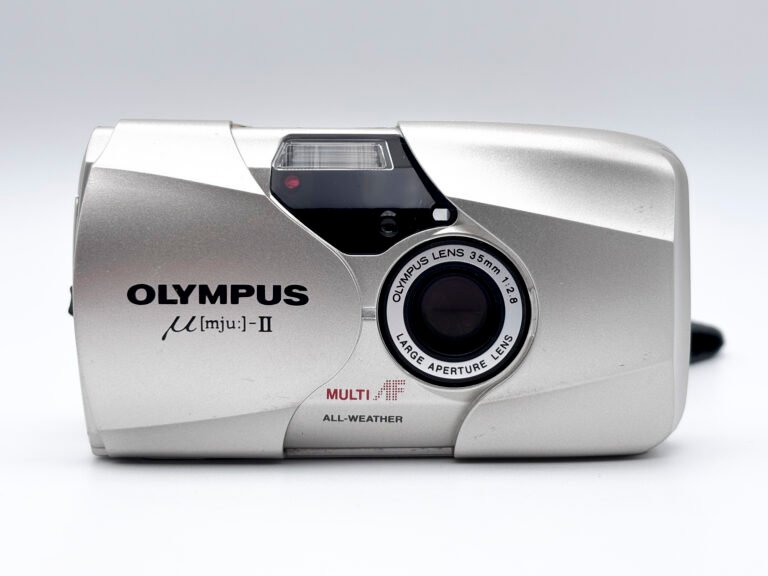 Olympus Mju II vu de face avec coque coulissante ouverte et objectif 35mm f/2.8 visible.