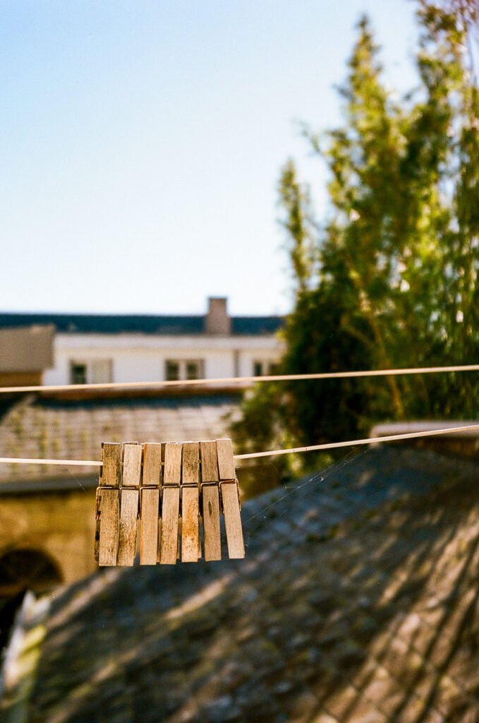 Pince à linge en bois suspendue sur un fil avec arrière-plan flou de toits et végétation.