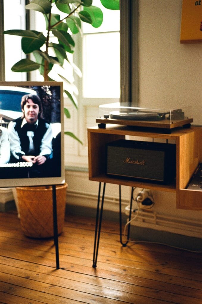 Tourne-disque et enceinte Marshall dans un salon lumineux avec un écran affichant un portrait.