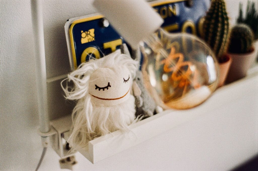 Petite poupée décorative posée sur une étagère blanche à côté d’objets du quotidien.