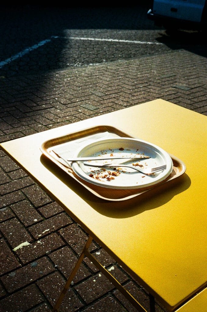 Plateau repas vide posé sur une table jaune en extérieur sous une lumière dure.
