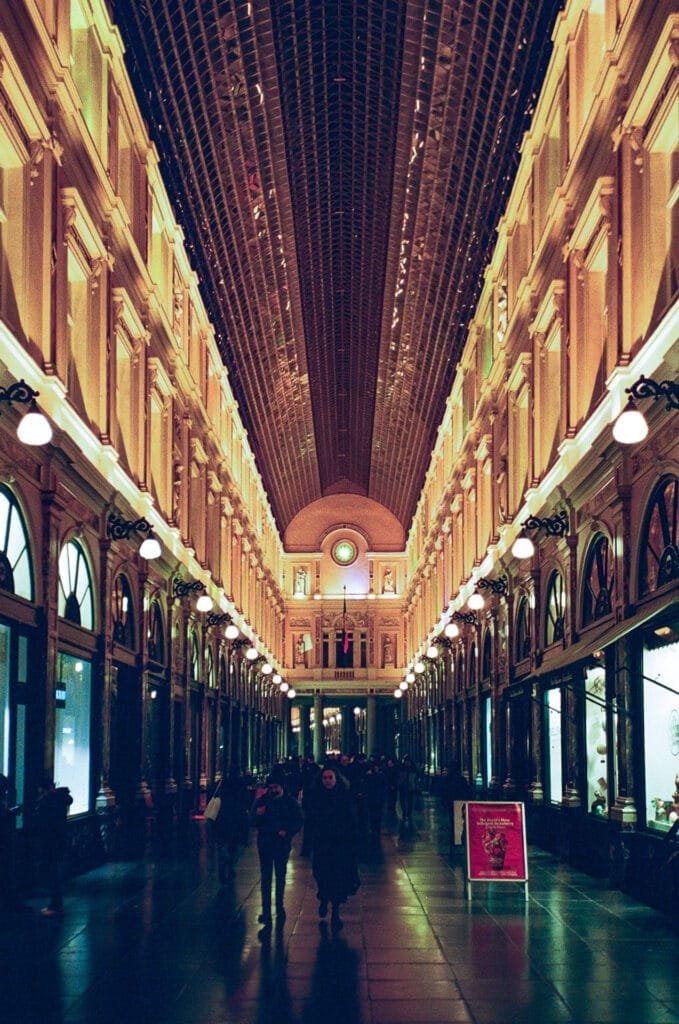 Intérieur des Galeries Saint-Hubert à Bruxelles éclairées par des lumières chaudes en fin de journée.