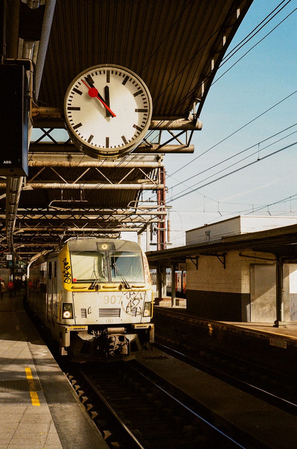 Train entrant en gare de Bruxelles-Midi sous une grande horloge, lumière d’hiver en fin de journée.
