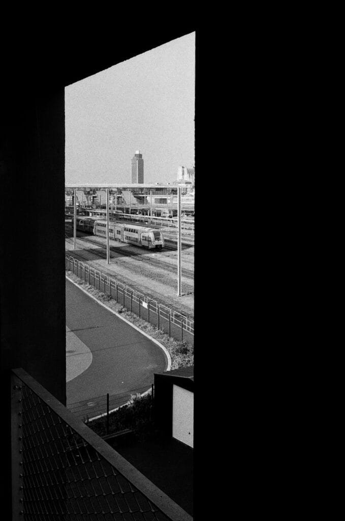Vue de la gare de Nantes et des voies ferrées, encadrée par une ouverture architecturale sombre créant un fort contraste graphique.