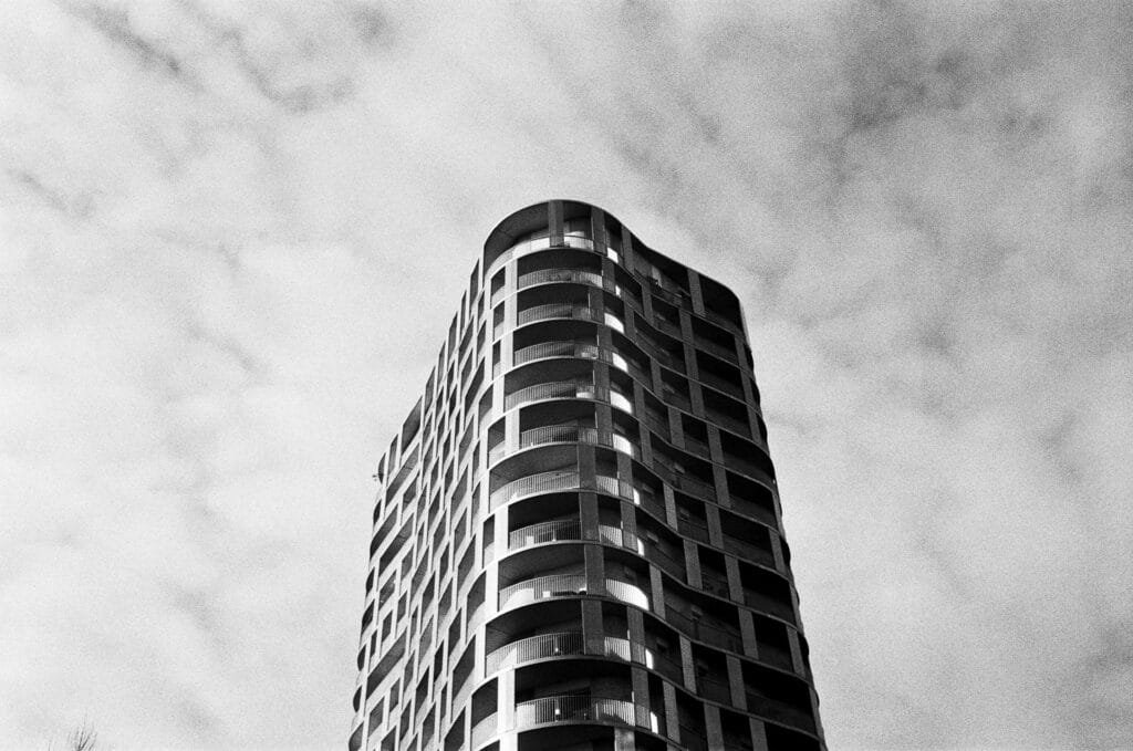 Immeuble contemporain photographié en contre-plongée, lignes courbes et balcons se détachant sur un ciel nuageux.