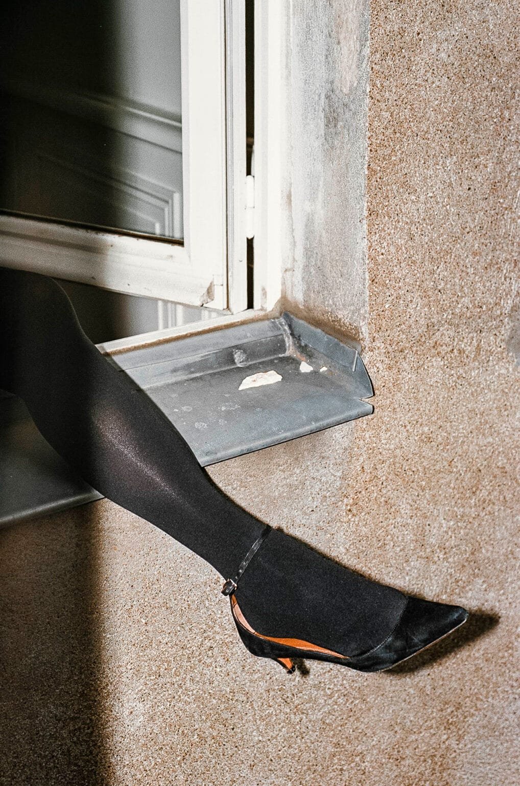 Jambe en collant noir et escarpin posée sur un rebord de fenêtre photographiée au flash à Nantes