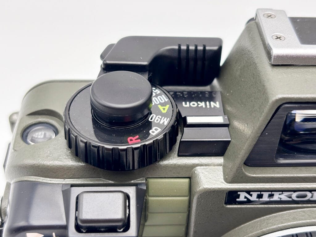 Levier d’armement replié et sélecteur de vitesses du Nikonos V, visibles sur le dessus du boîtier argentique amphibie.