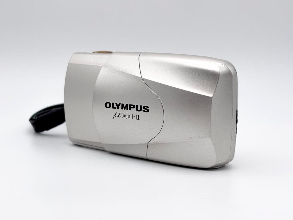 Olympus Mju II argent photographié en vue trois quarts avec coque coulissante fermée.