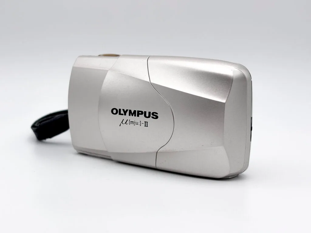 Olympus Mju II argent photographié en vue trois quarts avec coque coulissante fermée.