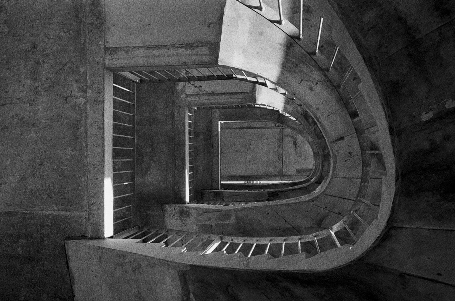 Escalier en béton du parking de la gare sud de Nantes, vu du dessus, lignes courbes et ombres en noir et blanc.