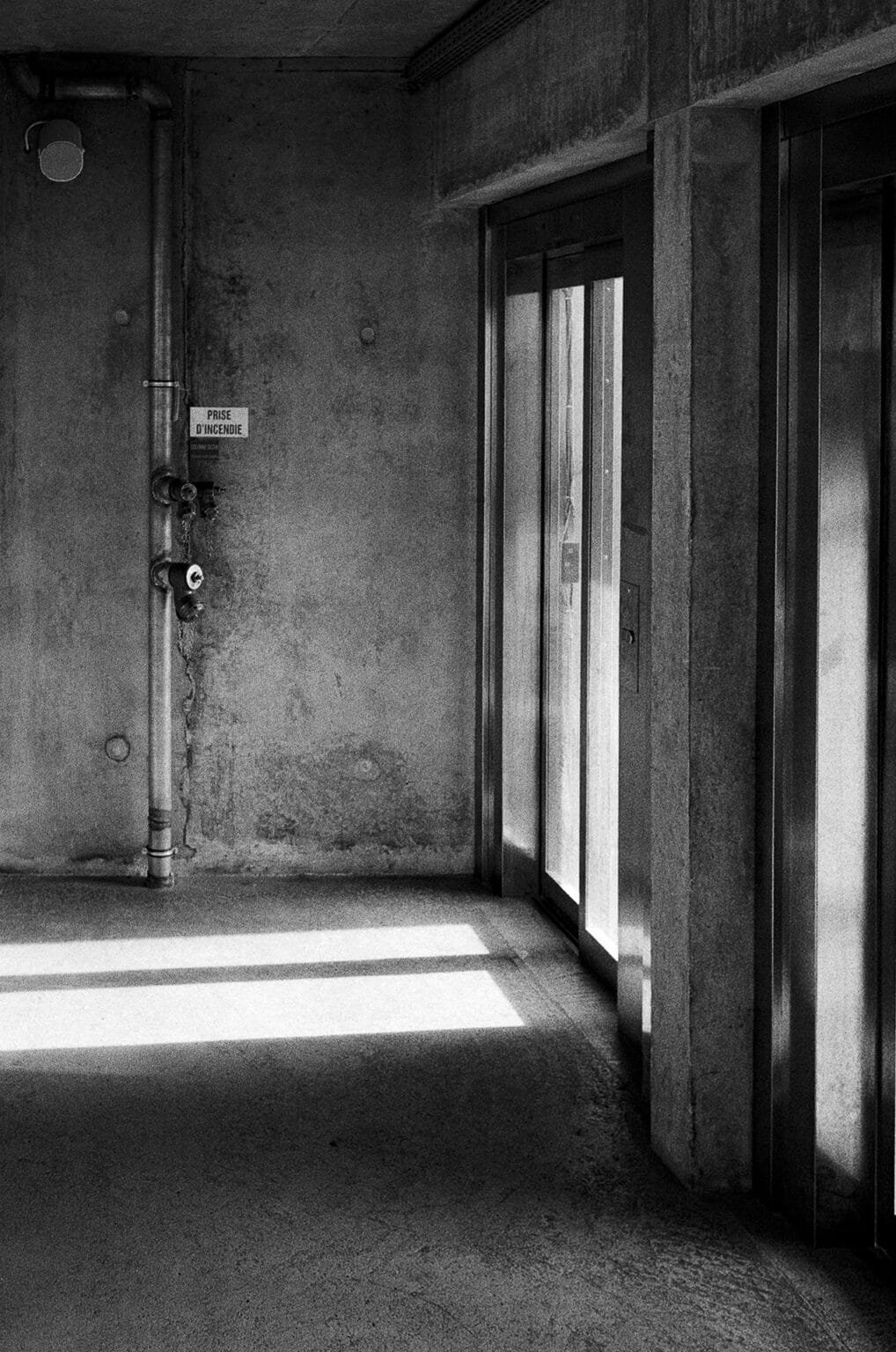 Jeu d’ombres et de lumière dans le parking de la gare sud de Nantes, murs en béton et portes vitrées en noir et blanc.