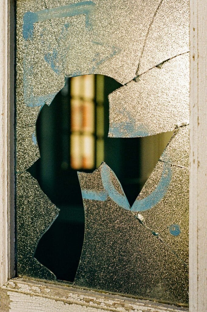 Vitre brisée en verre dépoli laissant apparaître une ouverture irrégulière sur un intérieur flou.