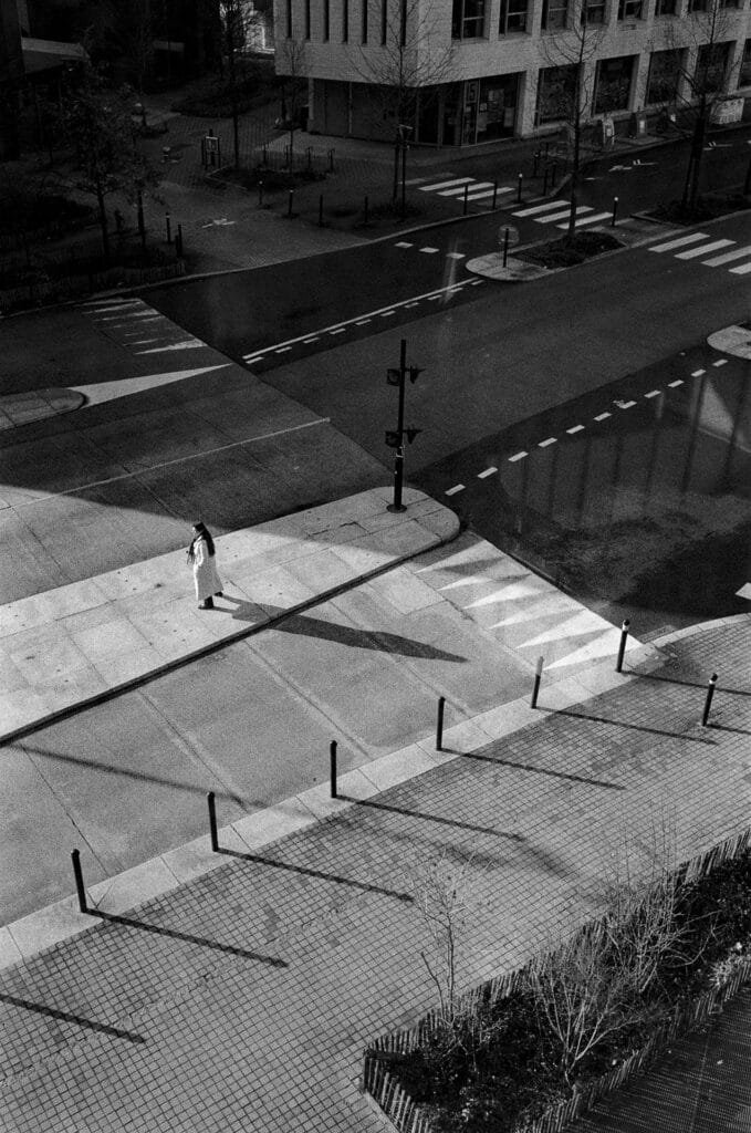 Vue plongeante sur un trottoir et un carrefour depuis le parking Gare Sud à Nantes, avec une silhouette isolée et de longues ombres.