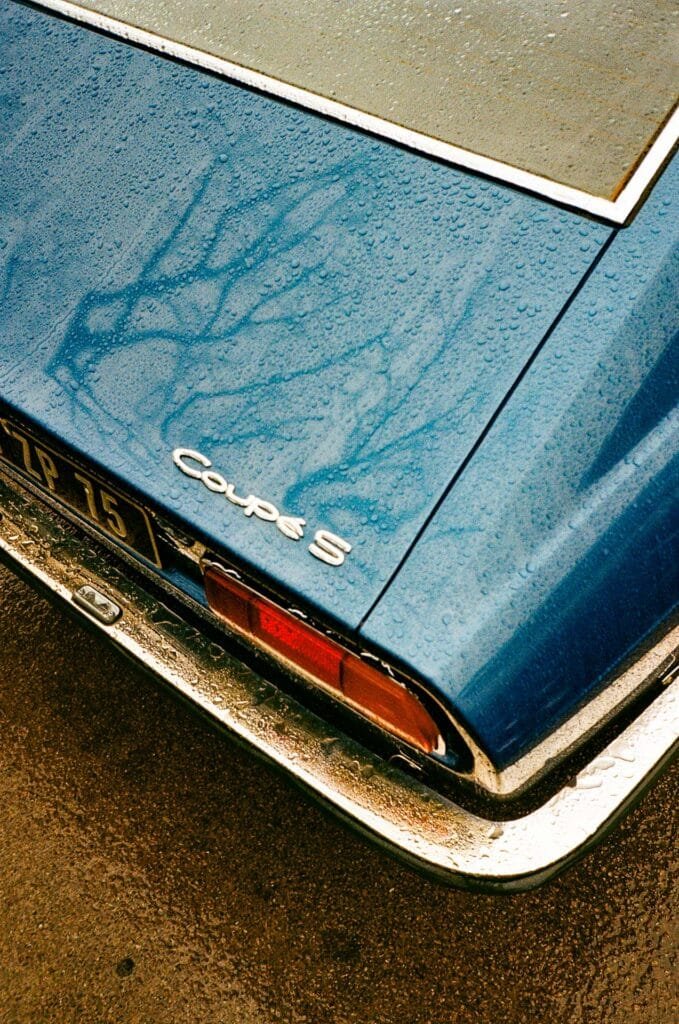 Arrière d’une Audi Coupé S bleue couverte de gouttes de pluie dans un parking à Nantes.