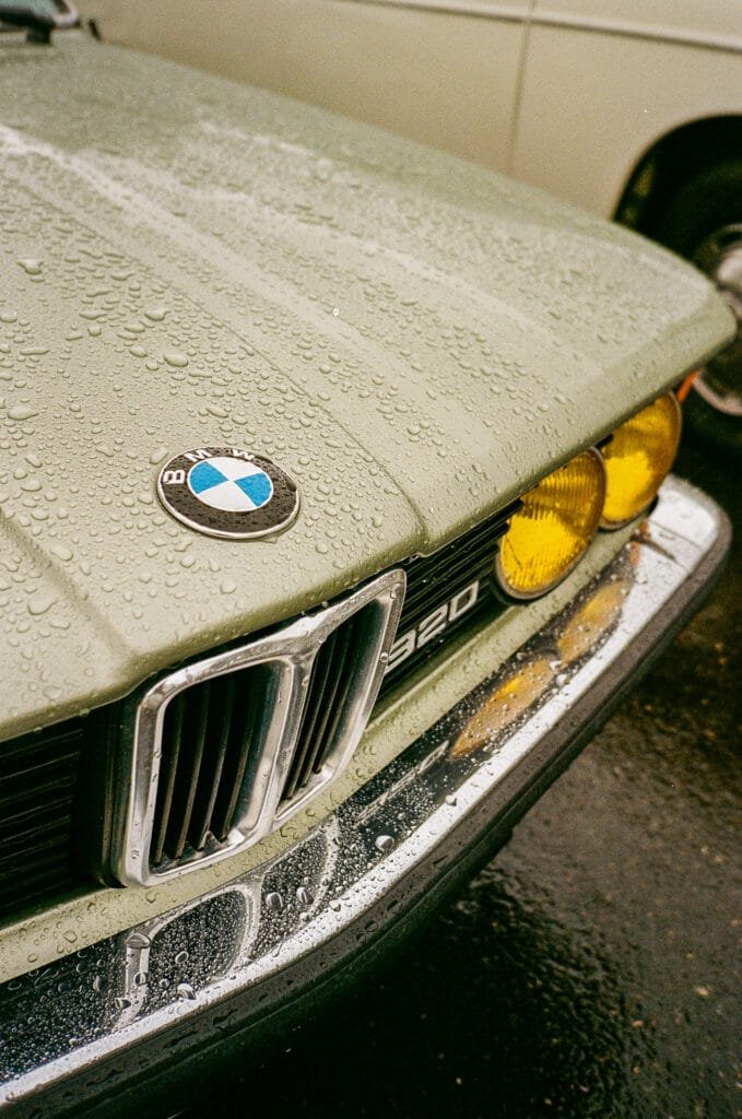 Avant d’une BMW 320 verte avec phares jaunes et gouttes de pluie, photographiée à Nantes.