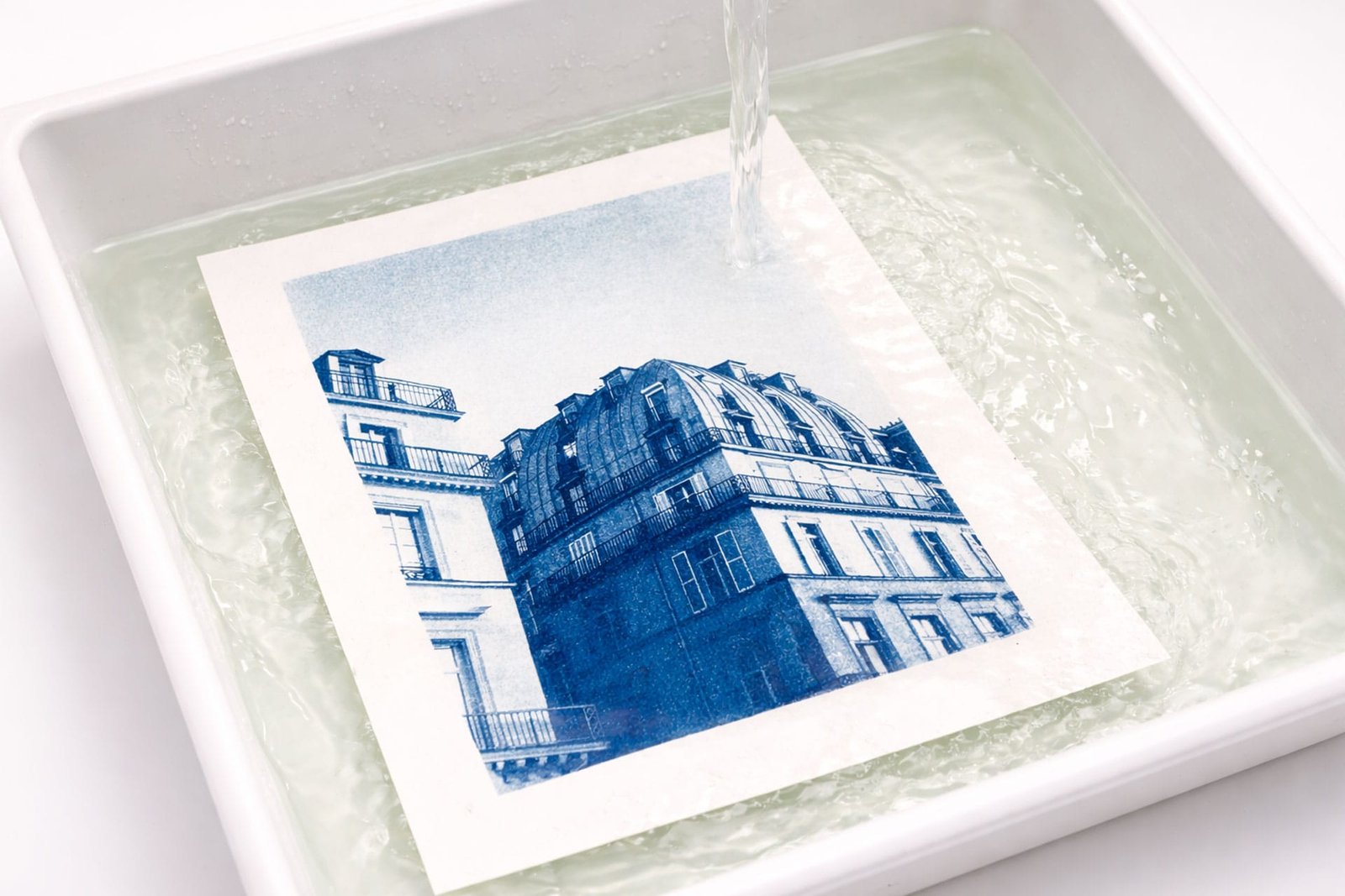 Cyanotype de la rue de Rivoli à Paris en cours de rinçage dans un bac d'eau, le bleu de Prusse apparaît progressivement