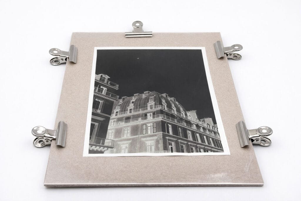 Transparent négatif cyanotype maintenu par des pinces sur un support, prêt pour l'insolation à la lampe UV