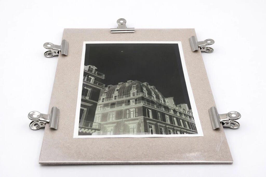 Transparent négatif cyanotype maintenu par des pinces sur un support, prêt pour l'insolation à la lampe UV