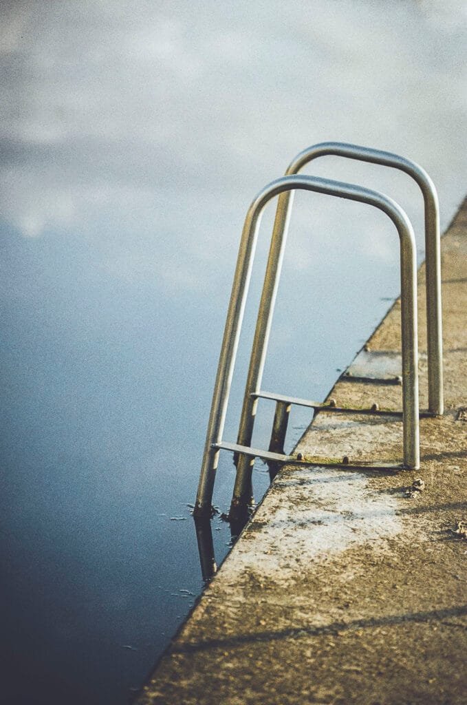Échelle métallique de la piscine du Prieuré à Dinard, eau calme et ciel nuageux en reflet, photo argentique Nikon F3