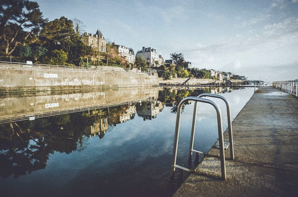 Vue large de la piscine du Prieuré à Dinard avec reflets des villas dans l'eau et échelle métallique au premier plan, photo argentique Nikon F3