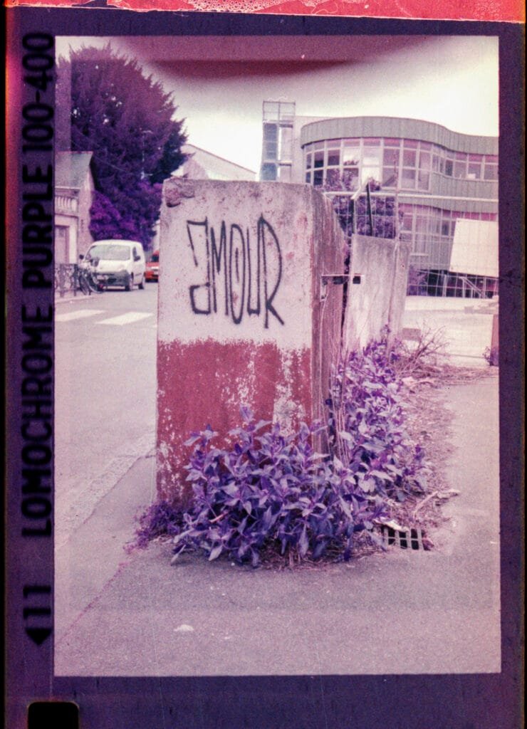 Graffiti "Amour" à l'envers sur un plot béton près du Jardin des Plantes à Nantes, photographié au Rollei A110 sur pellicule LomoChrome Purple 100-400
