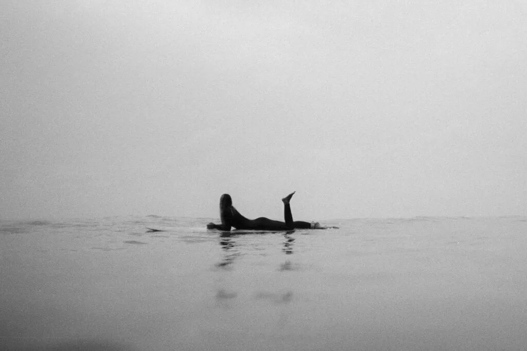 Surfeuse allongée sur sa planche dans un océan calme et brumeux, photo argentique noir et blanc minimaliste - © YannB / yannb.net