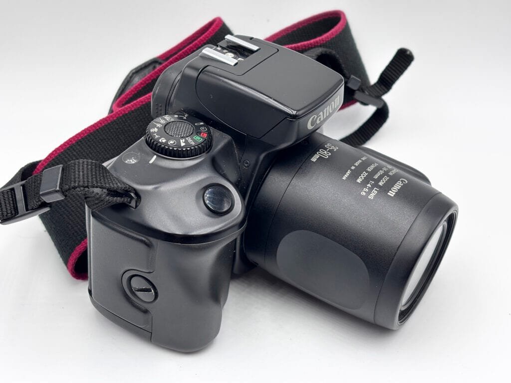 Canon EOS 700 argentique vu de trois quarts gauche, flash intégré et molette de modes visible