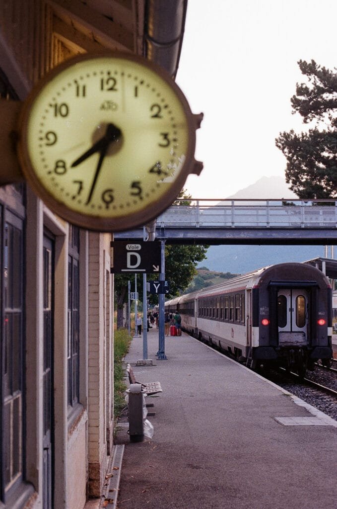 Ho@rloge de la gare d'Embrun au petit matin avec quai et train en arrière-plan, photo argentique au Nikon F6 sur Kodak Pro Image 100
