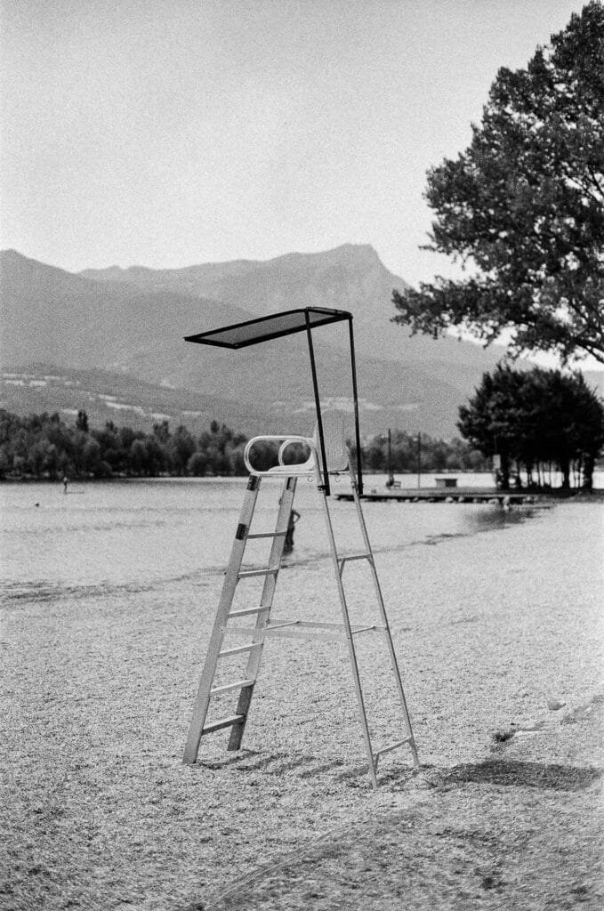 Chaise de surveillance de plage vide au bord du plan d'eau d'Embrun, avec les montagnes des Hautes-Alpes en arrière-plan, photographié en noir et blanc sur pellicule Ilford HP5 avec un Nikon F6