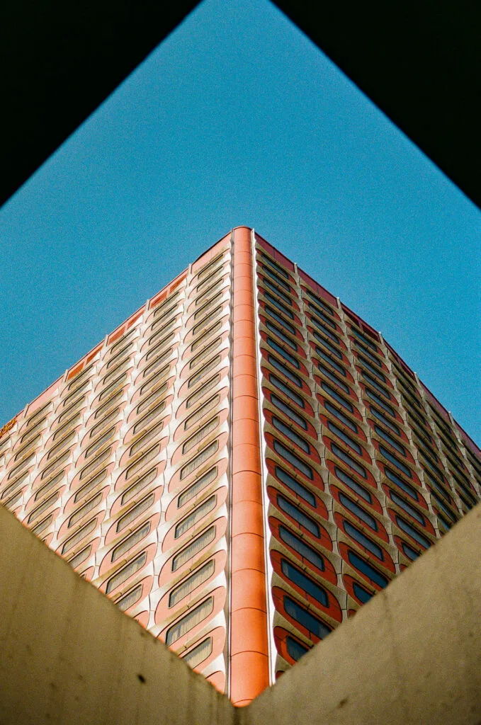 Angle de l'ancien hôtel Nikko cadré en losange entre deux murs de béton, ciel bleu, Kodak 200