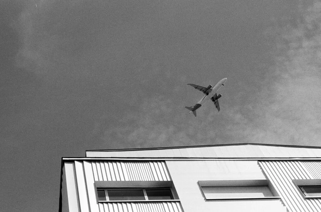 Avion en vol au-dessus d'un toit en diagonale et d'un bardage métallique vertical, Île de Nantes, argentique noir et blanc
